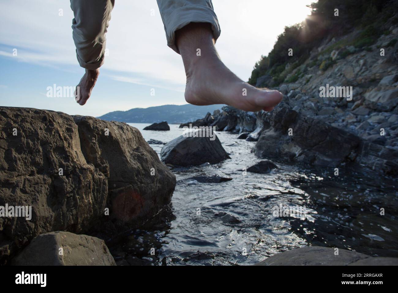 Angolo basso dei piedi dell'uomo che saltano tra le rocce sopra il torrente Foto Stock