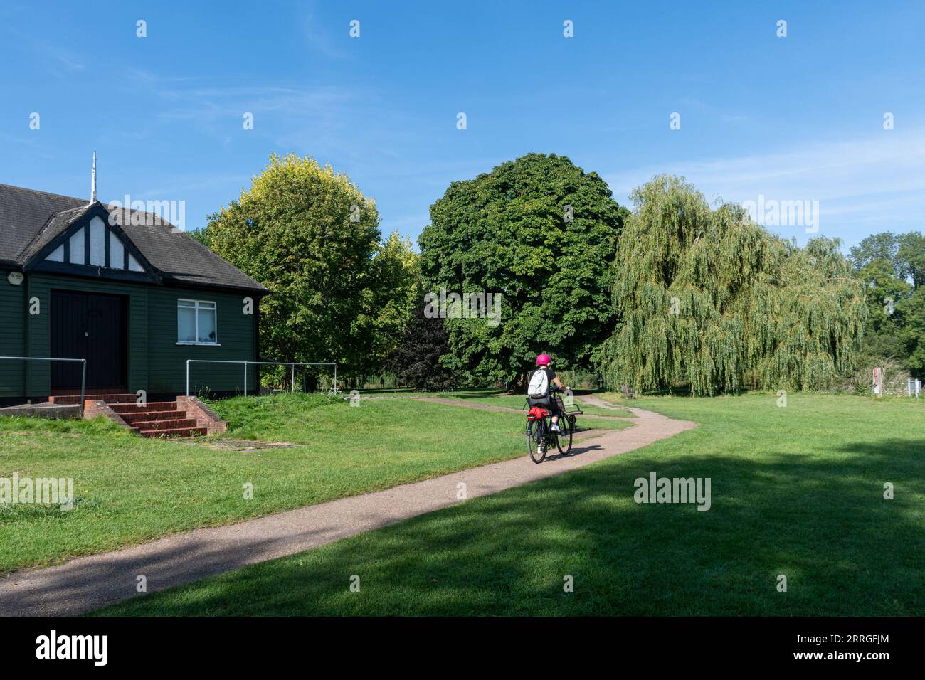 Ciclista che attraversa Runnymede Pleasure Grounds, Surrey, Inghilterra, Regno Unito, in una soleggiata mattinata estiva Foto Stock