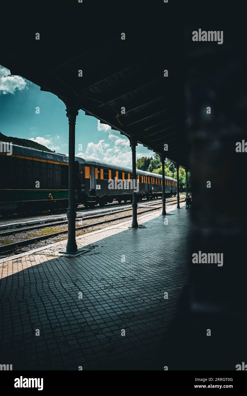 Una stazione ferroviaria vuota illuminata alla luce della sera quando un treno passa attraverso la stazione Foto Stock