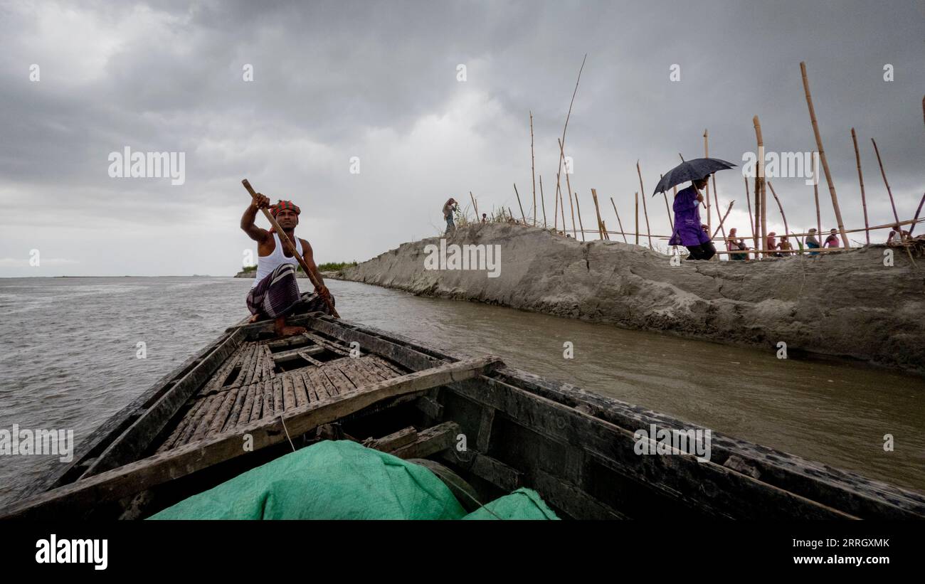 Rashed rema la sua barca di campagna a fianco degli abitanti del villaggio sul Kheyar Alga Char sul fiume Brahmaputra. L'ultima inondazione record ha invaso il char e ha lavato via tutti i loro raccolti e molte delle loro case. Da allora l'acqua è scesa, ma le colture sono sparite, così come grandi pezzi della loro terra. Foto Stock