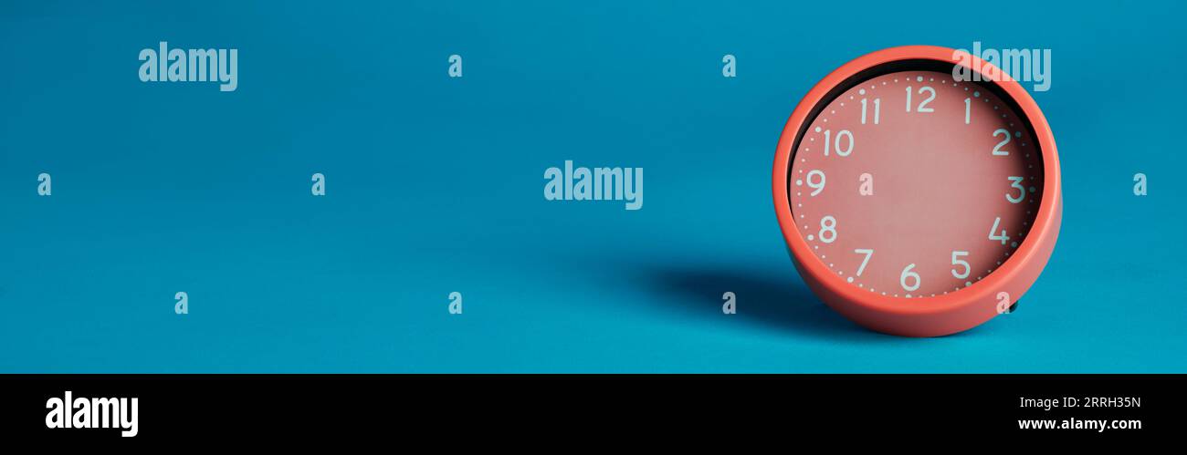 orologio rosa senza mani su sfondo blu con spazio vuoto a sinistra, in formato panoramico da utilizzare come banner web Foto Stock
