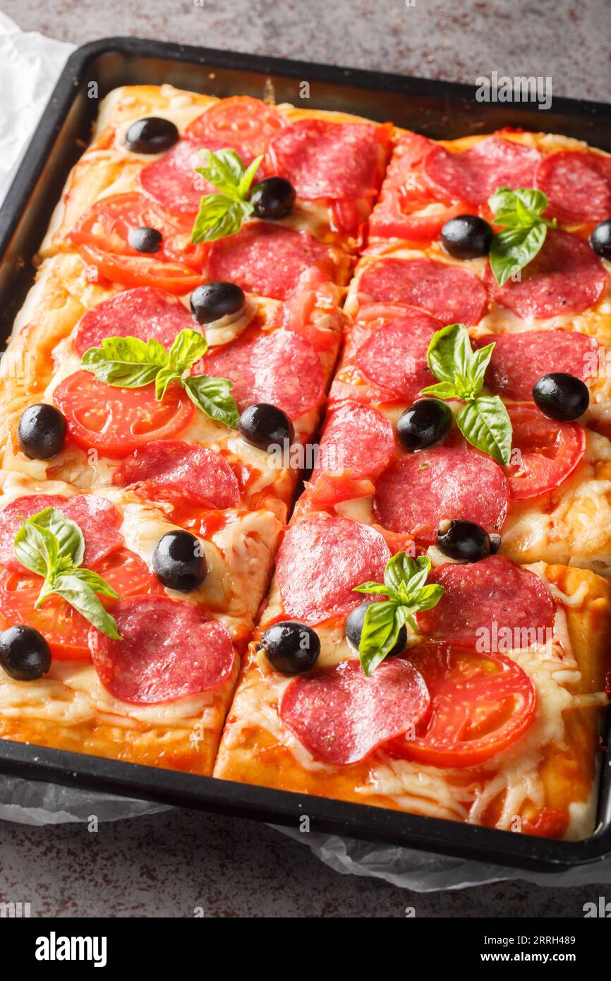 Pizza rettangolare con formaggio, salame, olive e pomodori da vicino in una  teglia da forno sul tavolo. Verticale Foto stock - Alamy