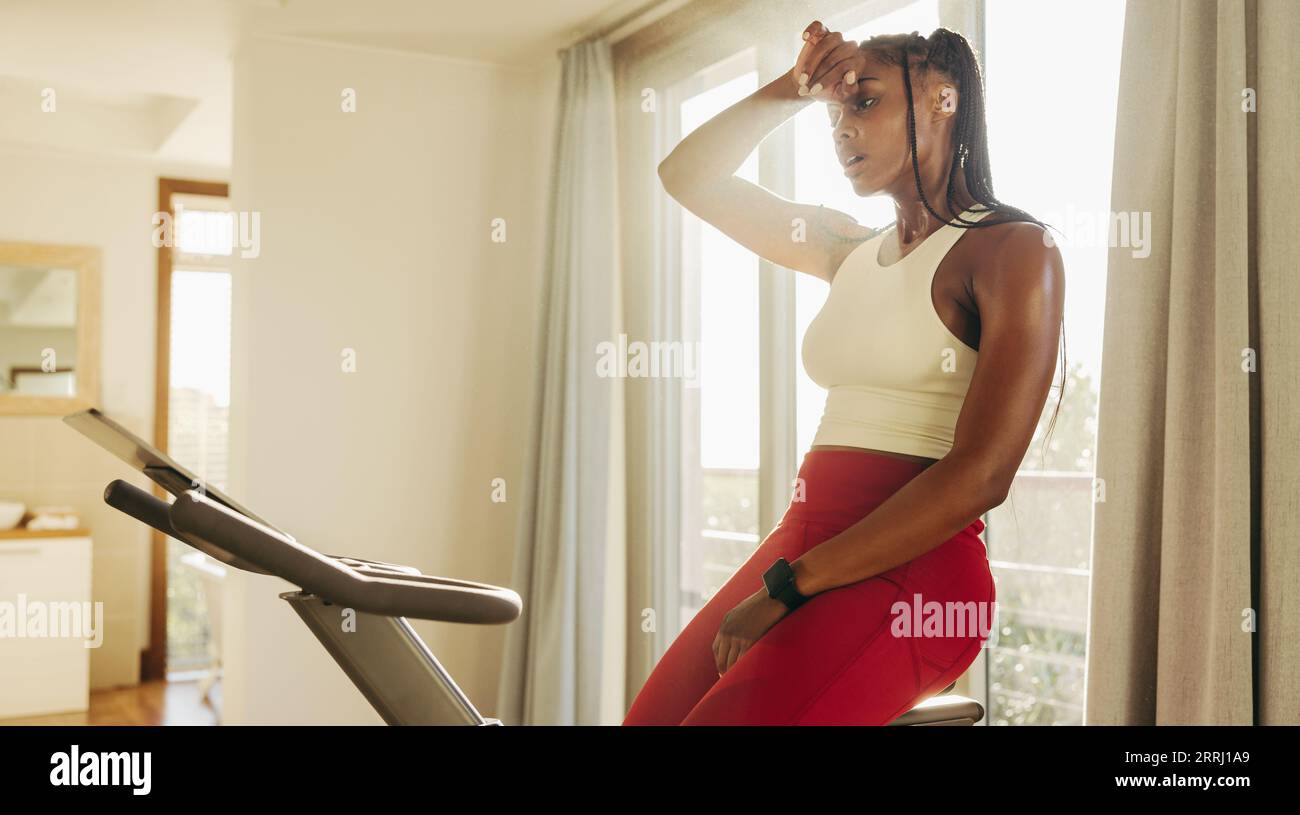 Una giovane donna afroamericana guidata si spinge ai suoi limiti su una cyclette digitale a casa, determinata a rimanere in forma e in salute attraverso regula Foto Stock