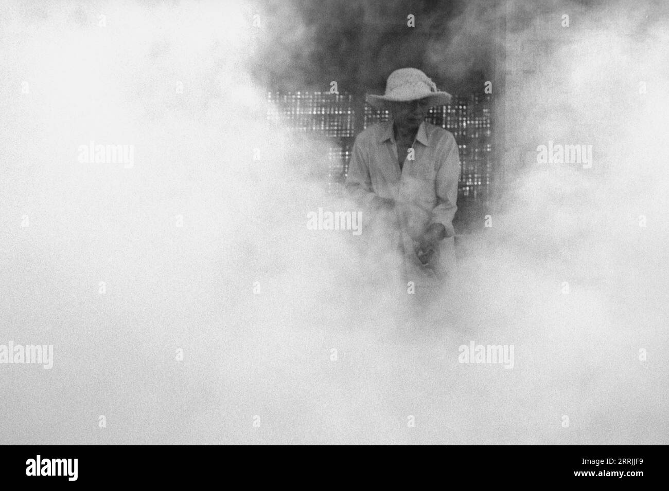 Ritratto di un contadino locale balinese circondato dal fumo mentre brucia rifiuti all'esterno nel campo Foto Stock