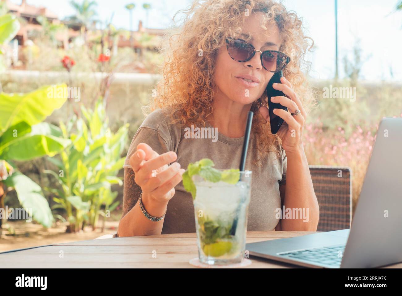 Nuovo concetto di ufficio di lavoro moderno online. Una donna che lavora ovunque come nomade digitale. Libertà di ufficio. Vita freelance alternativa. Donna adulta che usa il computer portatile e chiama con il telefono Foto Stock