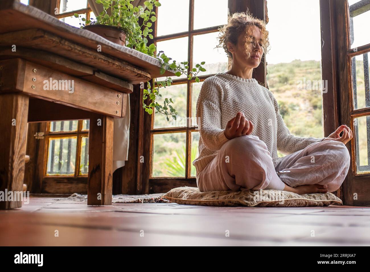 Concetto di stile di vita sano con donna adulta che fa posizione yoga lotys a casa. Salute asana benessere mentale positivo. Meditazione zen come esercizio fisico seduto sul pavimento a casa. Attività mattutina da sola Foto Stock