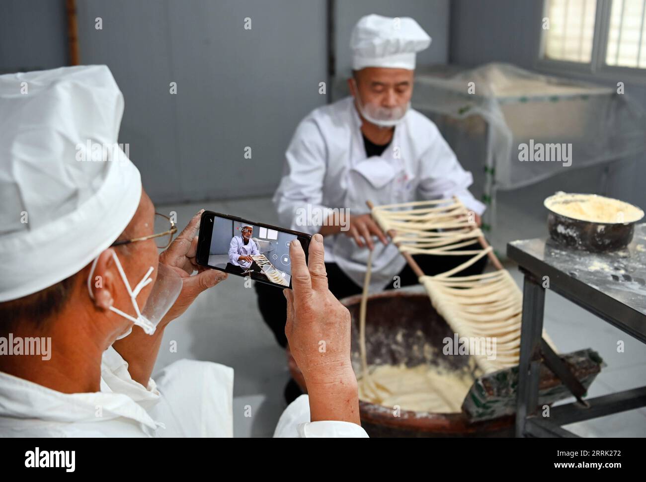 220817 -- LUONAN, 17 agosto 2022 -- li Changman L prende un video mentre suo figlio li Nianping sta facendo spaghetti vuoti nel villaggio di Meidi di Bao An Township nella contea di Luonan della città di Shangluo, nella provincia dello Shaanxi della Cina nord-occidentale, 16 agosto 2022. Li Changman, un abitante di 66 anni del villaggio di Meidi, ha imparato le abilità uniche di produzione di noodle cave da quando era adolescente. È l'erede delle abilità luonane fatte a mano per la produzione di noodle hallow che è elencato come patrimonio culturale immateriale provinciale. Incoraggiò suo figlio a imparare questa abilità, e insegnò anche le abilità agli abitanti del villaggio per aumentare la loro io Foto Stock