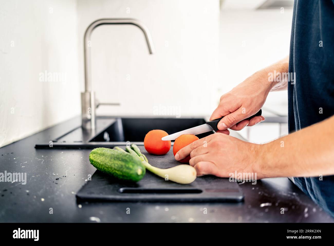 Tagliare l'insalata con un coltello affilato. Uomo che cucina. Tritare i pomodori e le verdure. Prepara il cibo nella cucina casalinga. Pasto vegetariano sano. Foto Stock