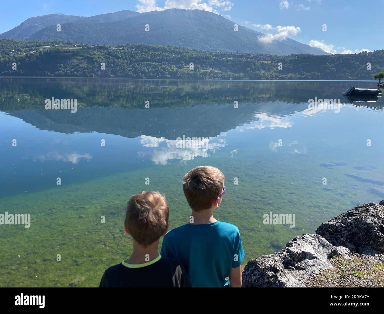 Due ragazzi che guardano il tranquillo Lago di Caldonazzo in Trentino, il Lago di Caldonazzo, la Suganertal, la Valsugana, il Lago di Levico, lago di Levico, natura, acqua, montagna, attività, sole, nuvole, Caldonazzo, Trentino alto Adige, Italia Foto Stock