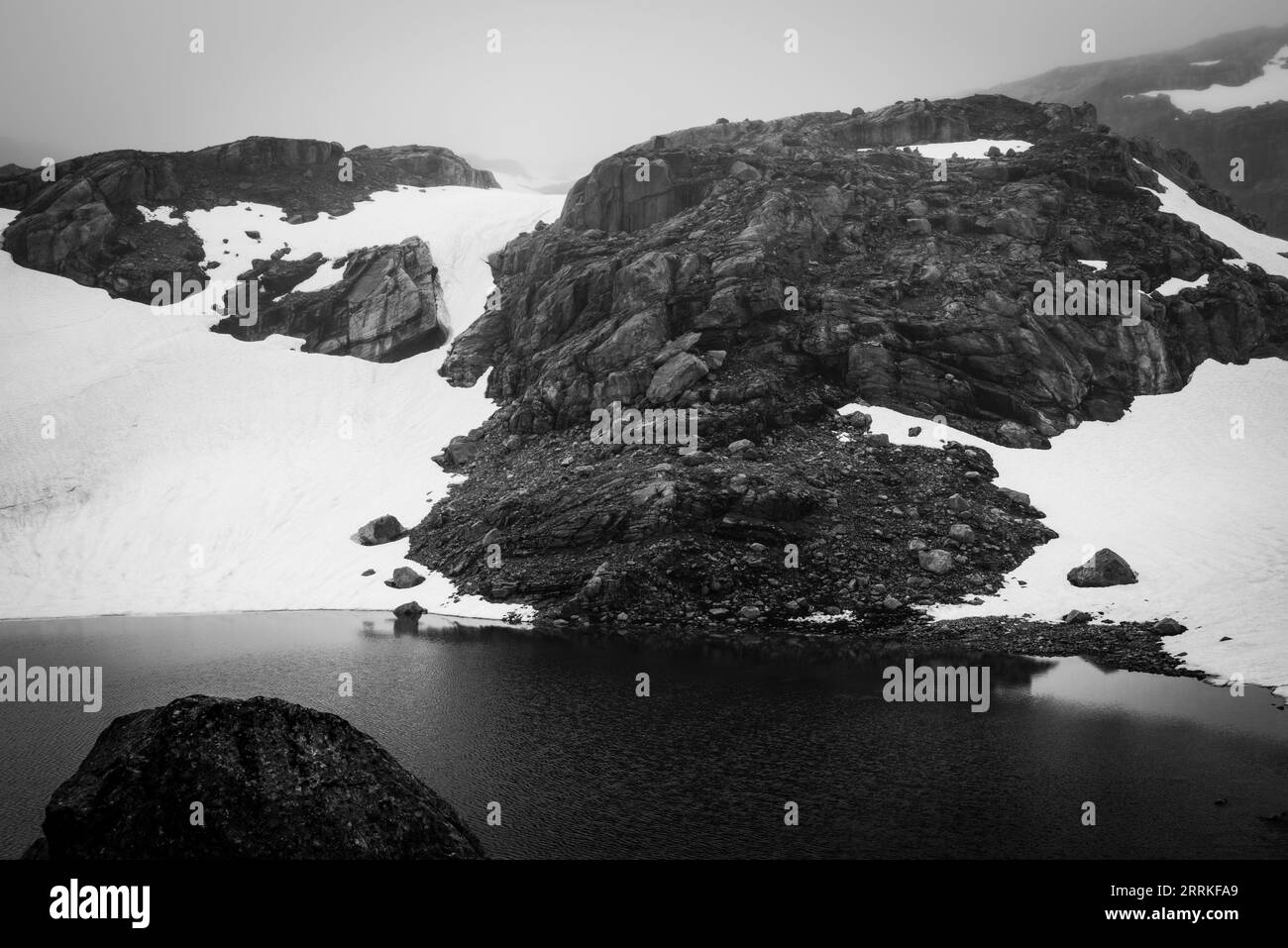 Un tarn riflette la neve residua dell'estate nel Parco Nazionale di Folgefonna, Vestland, Norvegia. Foto Stock