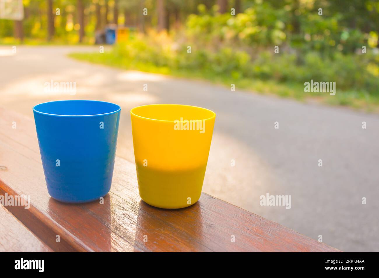 Tazze blu e gialle con caffè al sole del mattino. Colori ucraini patriottici. Due tazze di plastica con cappuccino. Tazze da campeggio portatili. Foto Stock
