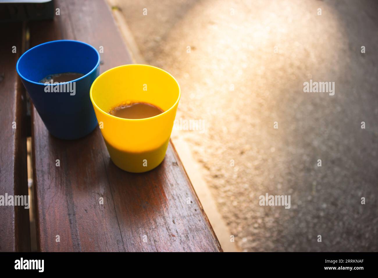 Tazze blu e gialle con caffè al sole del mattino. Colori ucraini patriottici. Due tazze di plastica con cappuccino. Tazze da campeggio portatili. Foto Stock