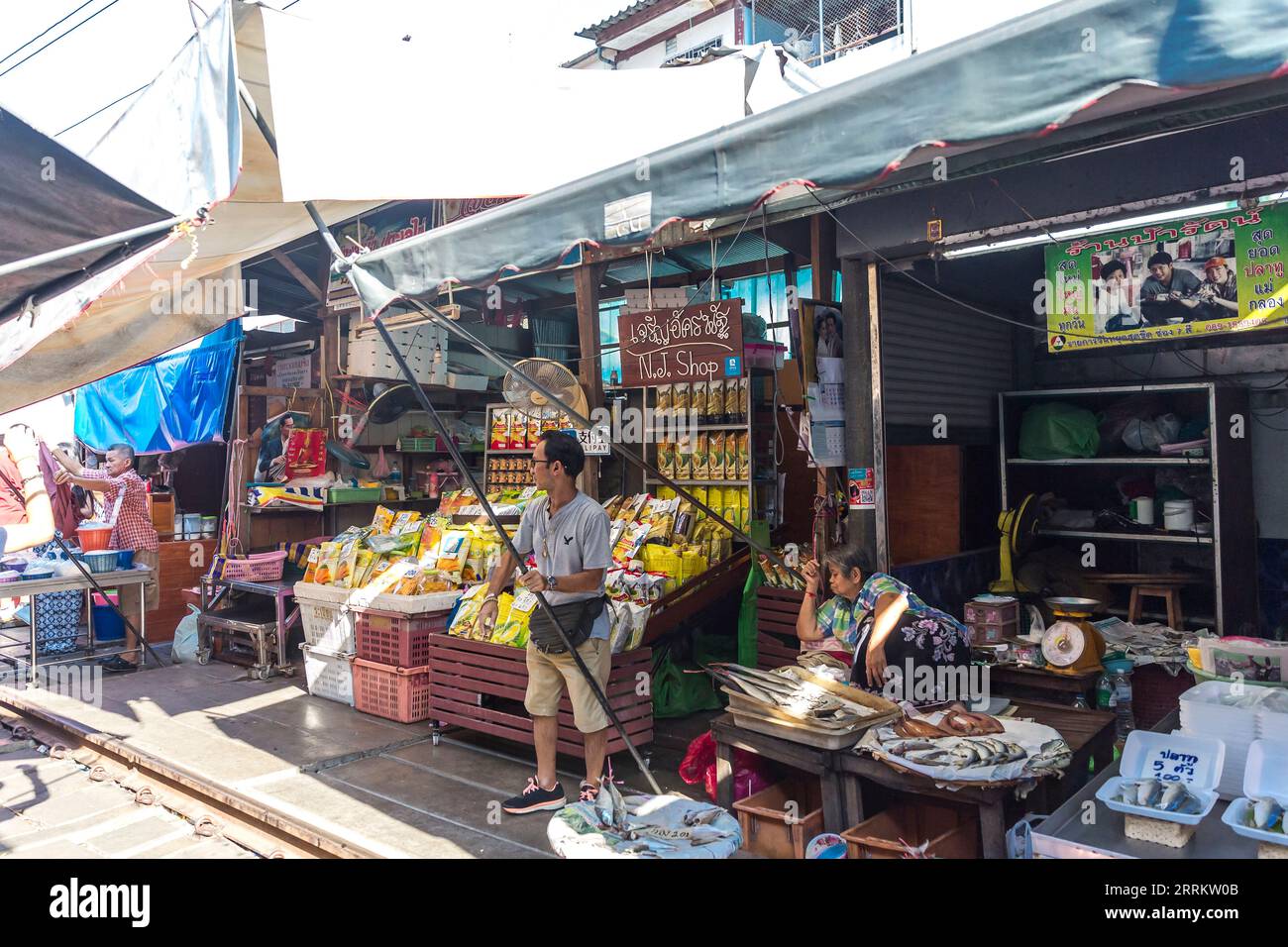 I venditori spostano le loro merci e si mettono in pari con le tende da sole quando arriva un treno, vendendo cibo sulle rotaie, il mercato ferroviario di Maeklong, il mercato ferroviario di Talad Rom Hub, vicino a Bangkok, Samut Songkhram, Thailandia, Asia Foto Stock