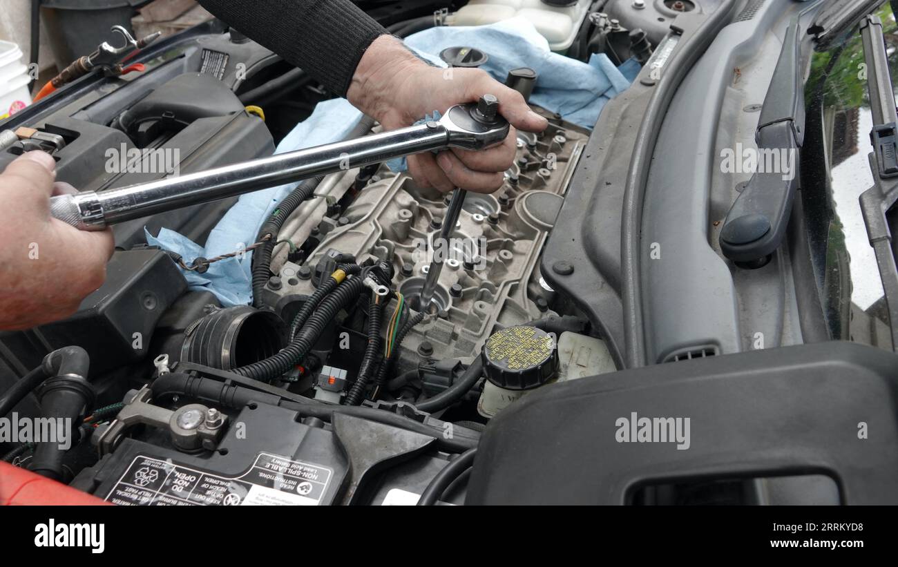 Vista, CA USA - 3 settembre 2023: Primo piano delle mani di un uomo anziano che stringono la nuova candela sul motore Volvo Foto Stock