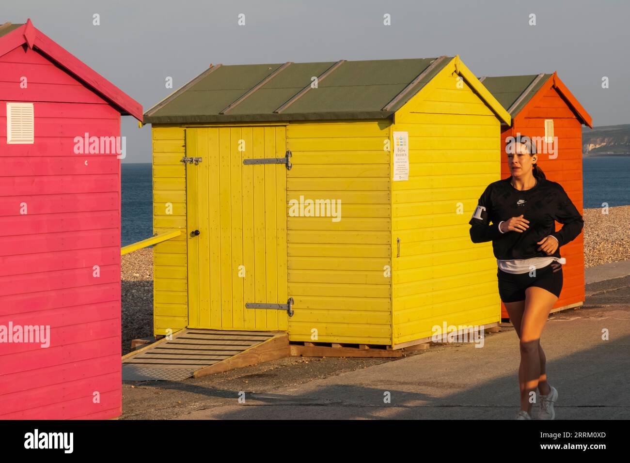 Inghilterra, Sussex, East Sussex, Seaford, colorati rifugi sul lungomare e jogger di prima mattina Foto Stock