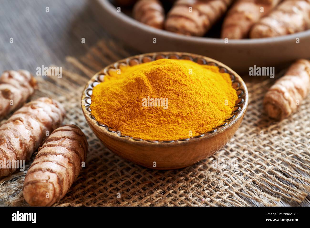 Polvere di curcuma in una ciotola di legno, con radice fresca sullo sfondo Foto Stock