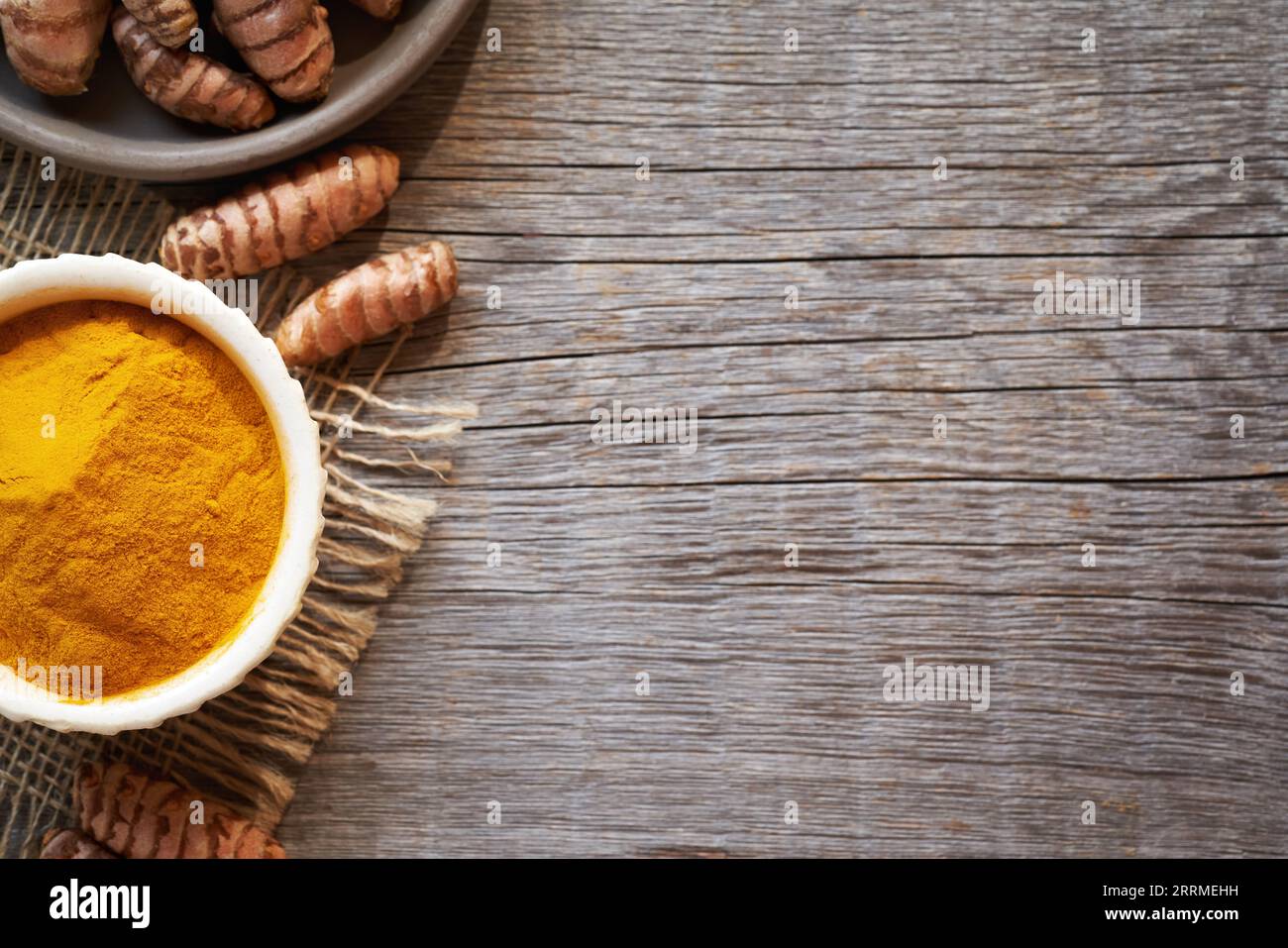 Polvere di curcuma in una ciotola con radice di curcuma fresca su uno sfondo di legno con spazio per la copia Foto Stock