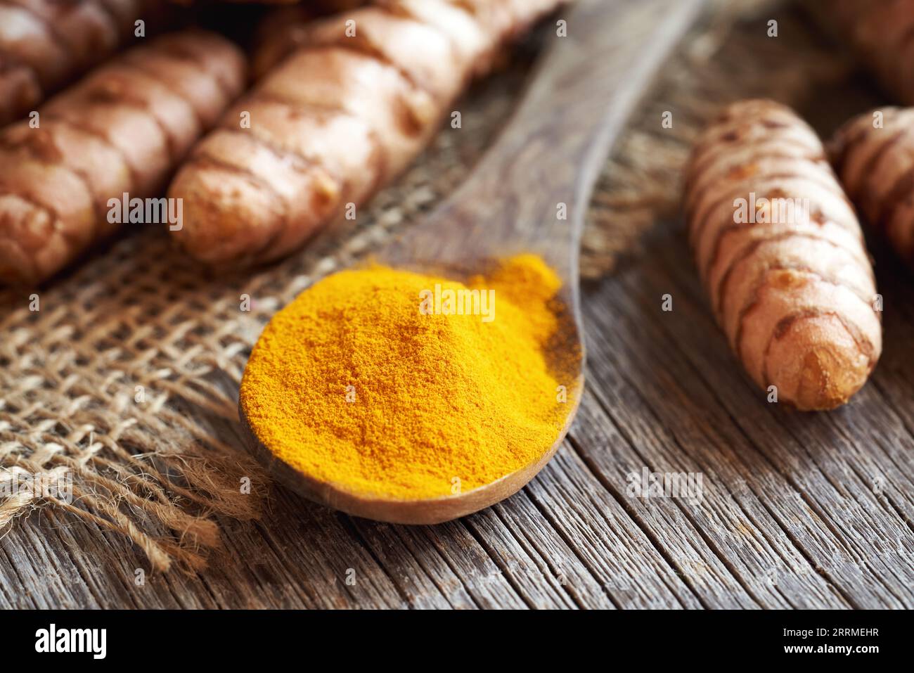 Macinare la curcuma in polvere su un cucchiaio su un tavolo, con radice fresca sullo sfondo Foto Stock