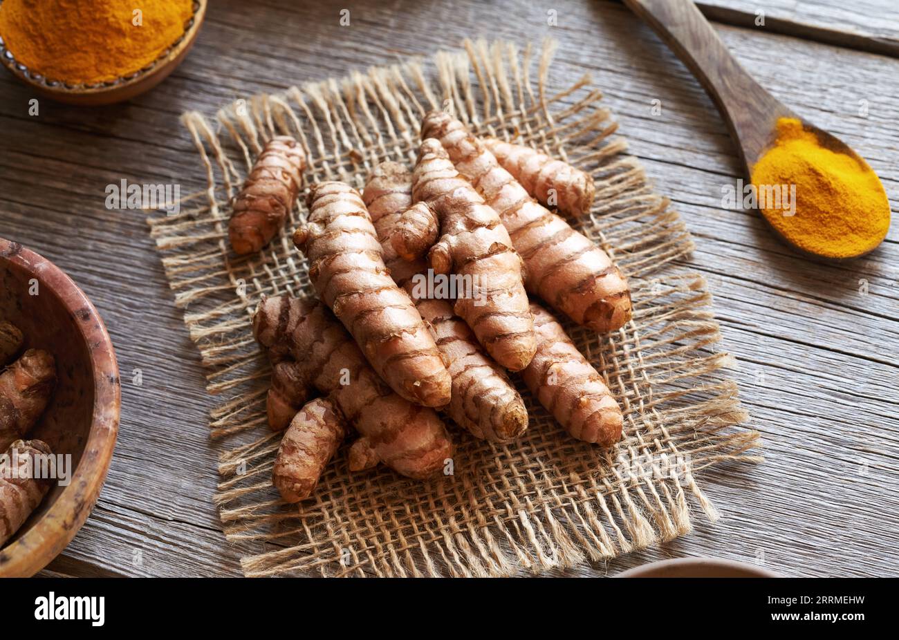 Radice di curcuma fresca o rizomi su un tavolo con polvere di curcuma essiccata sullo sfondo Foto Stock