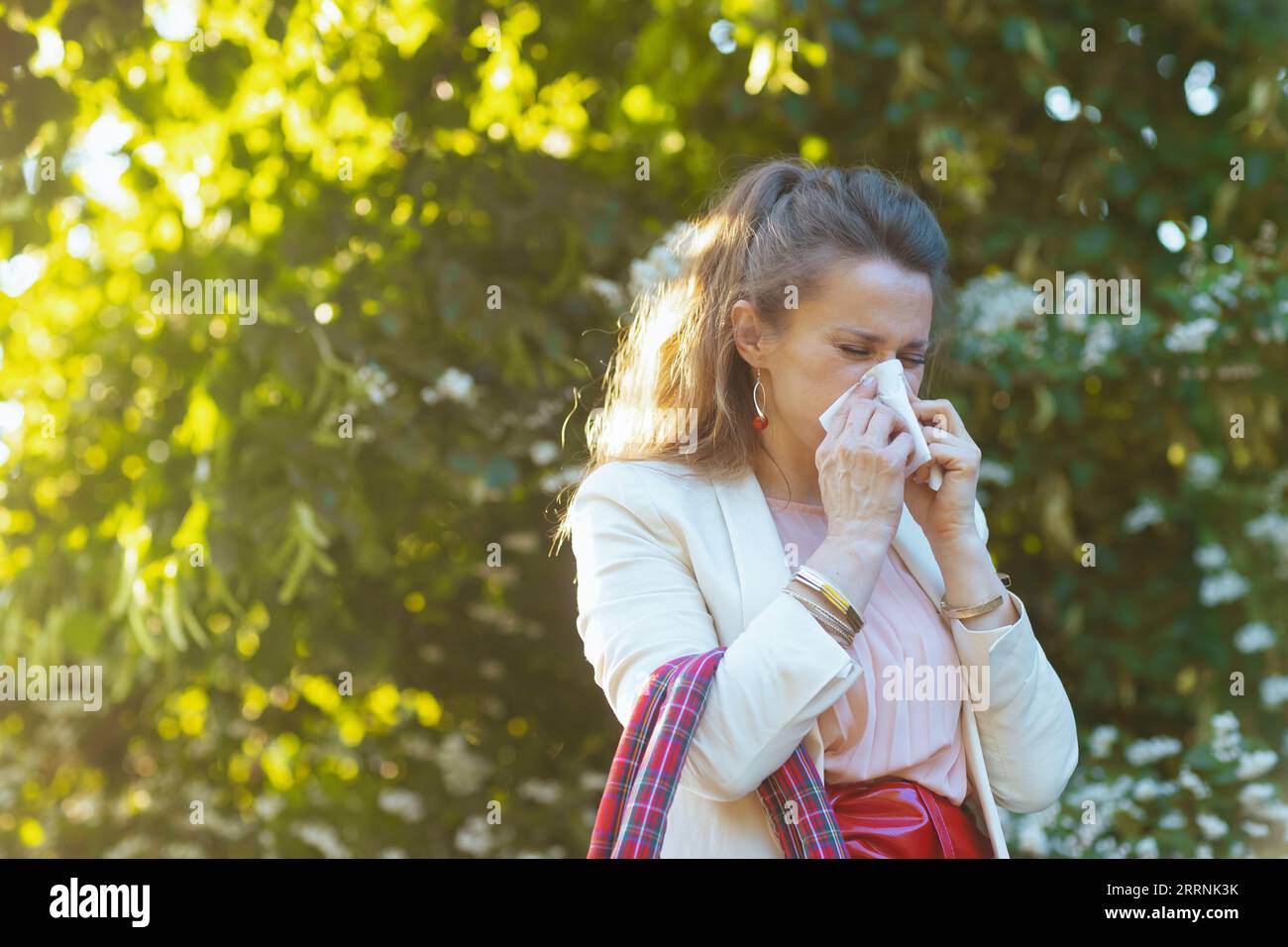 elegante donna in abito rosa e giacca bianca in città con tovagliolo ha un attacco allergico. Foto Stock