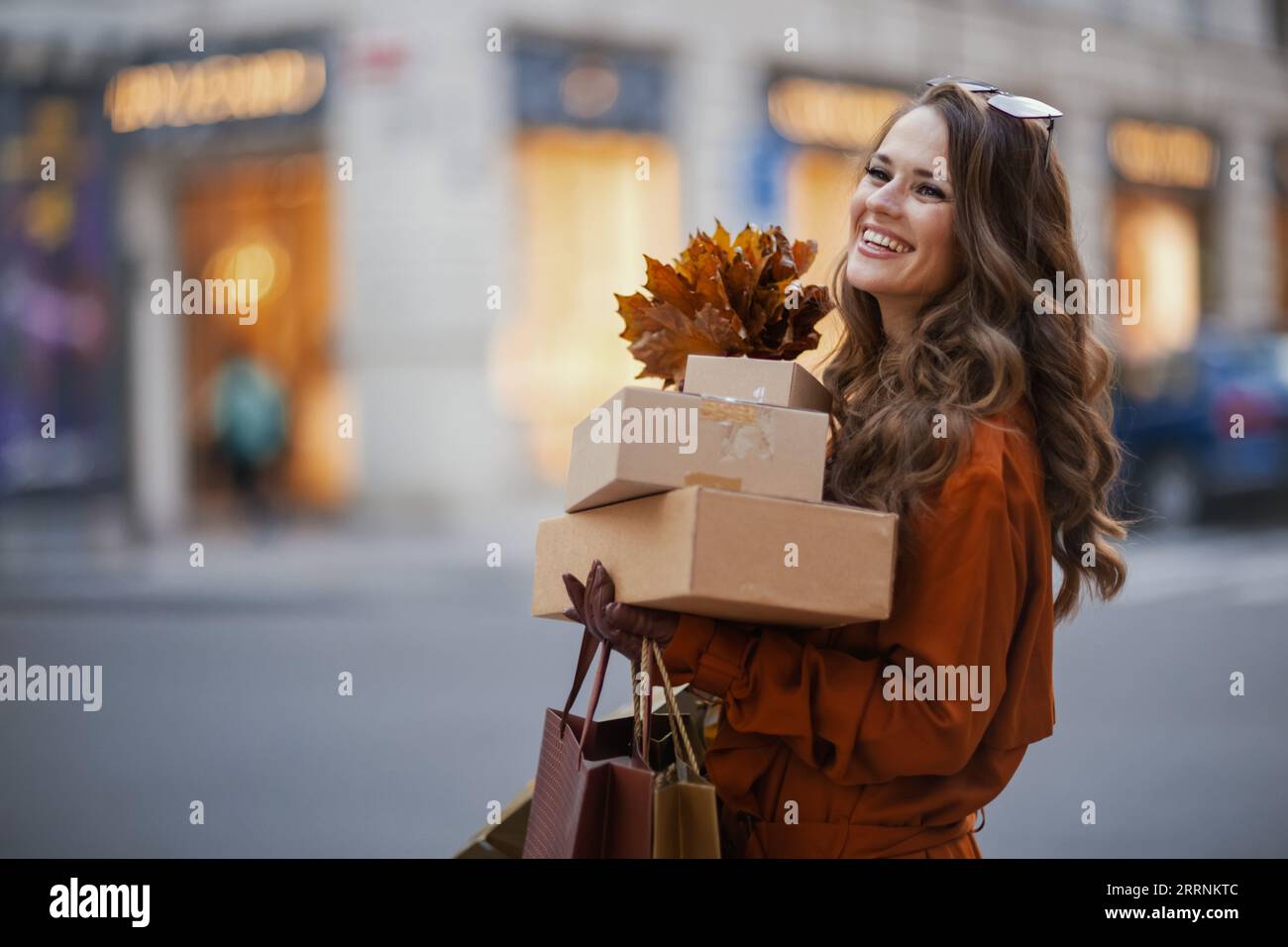Ciao ottobre. giovane donna sorridente in trench arancione con pacchi, borse della spesa e foglie gialle autunnali in città. Foto Stock
