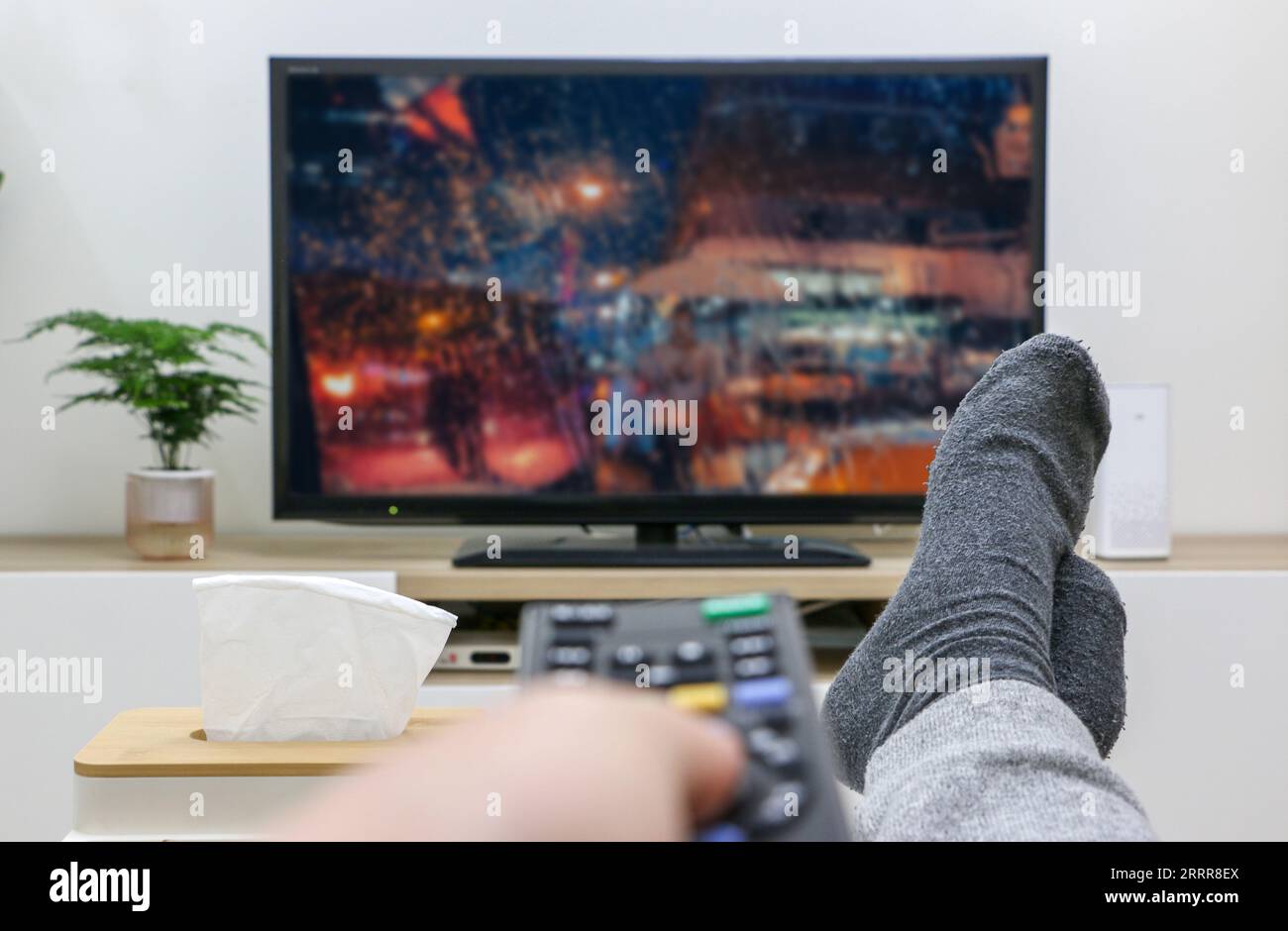 Concetto di giornata piovosa, piedi in alto a casa, telecomando TV, visione in prima persona in streaming e visione dello schermo televisivo. Foto Stock