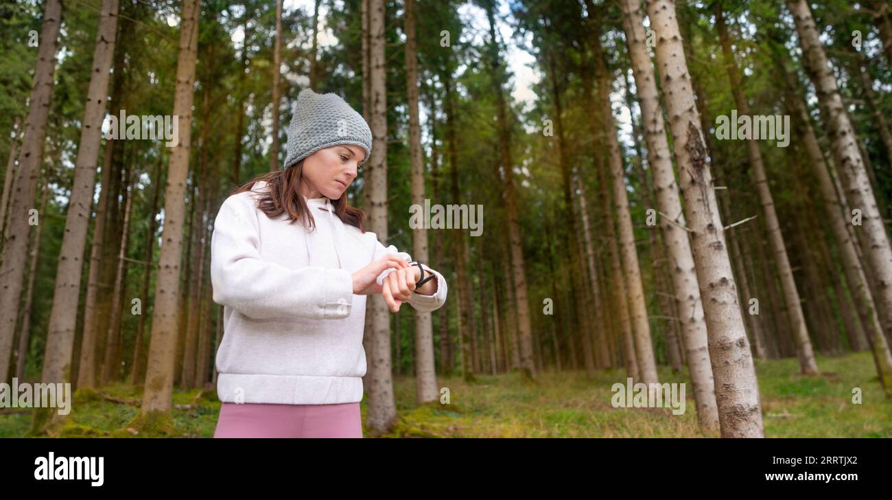 Vesti la donna sportiva controllando il suo orologio intelligente fitness tracker, sfondo forestale. Foto Stock