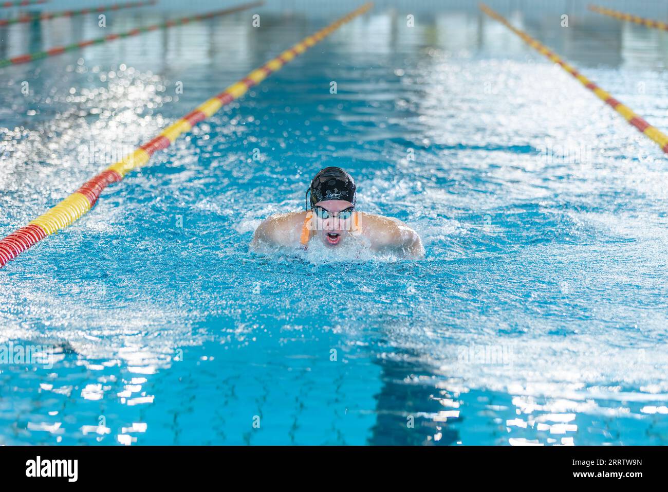 Nuotatore competitivo femminile che si muove attraverso l'acqua eseguendo il colpo di farfalla durante l'allenamento di nuoto, vista frontale. Foto Stock