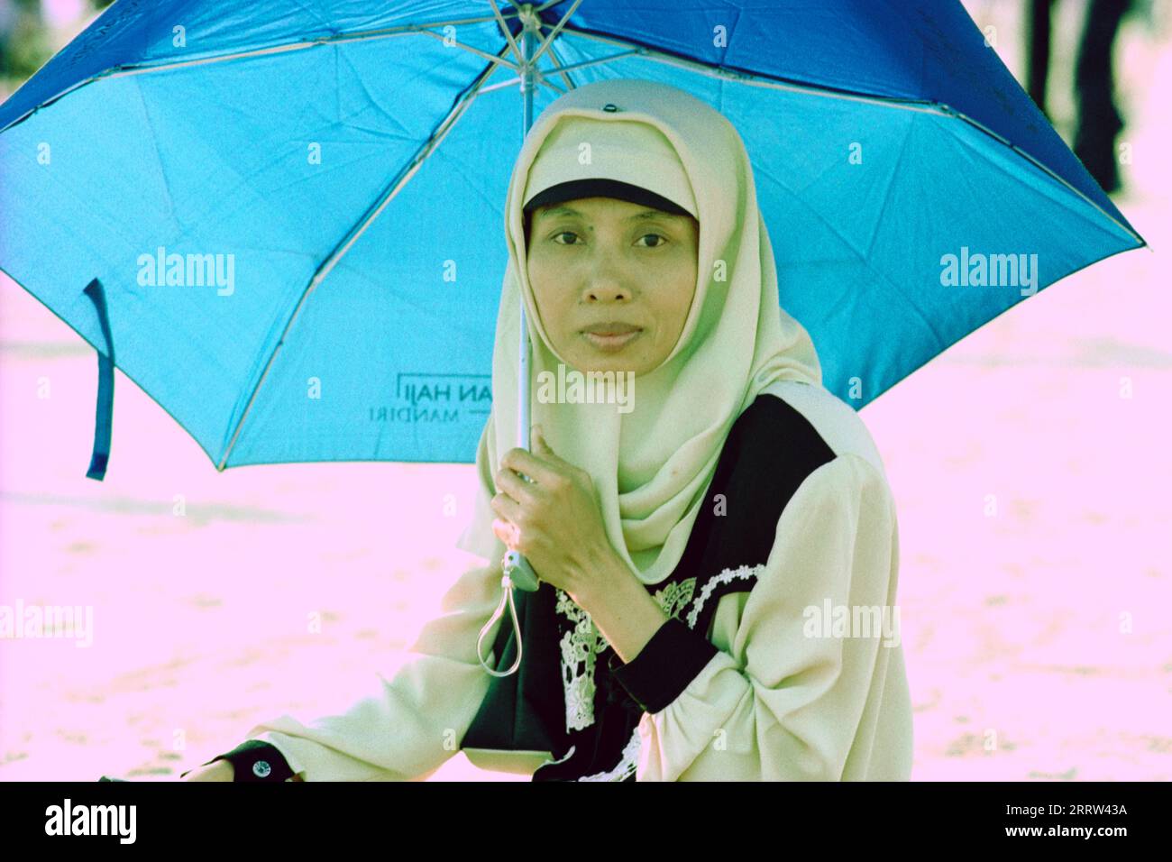 Giovane donna musulmana che indossa un velo seduto sotto un ombrello che si nasconde dal sole caldo Foto Stock
