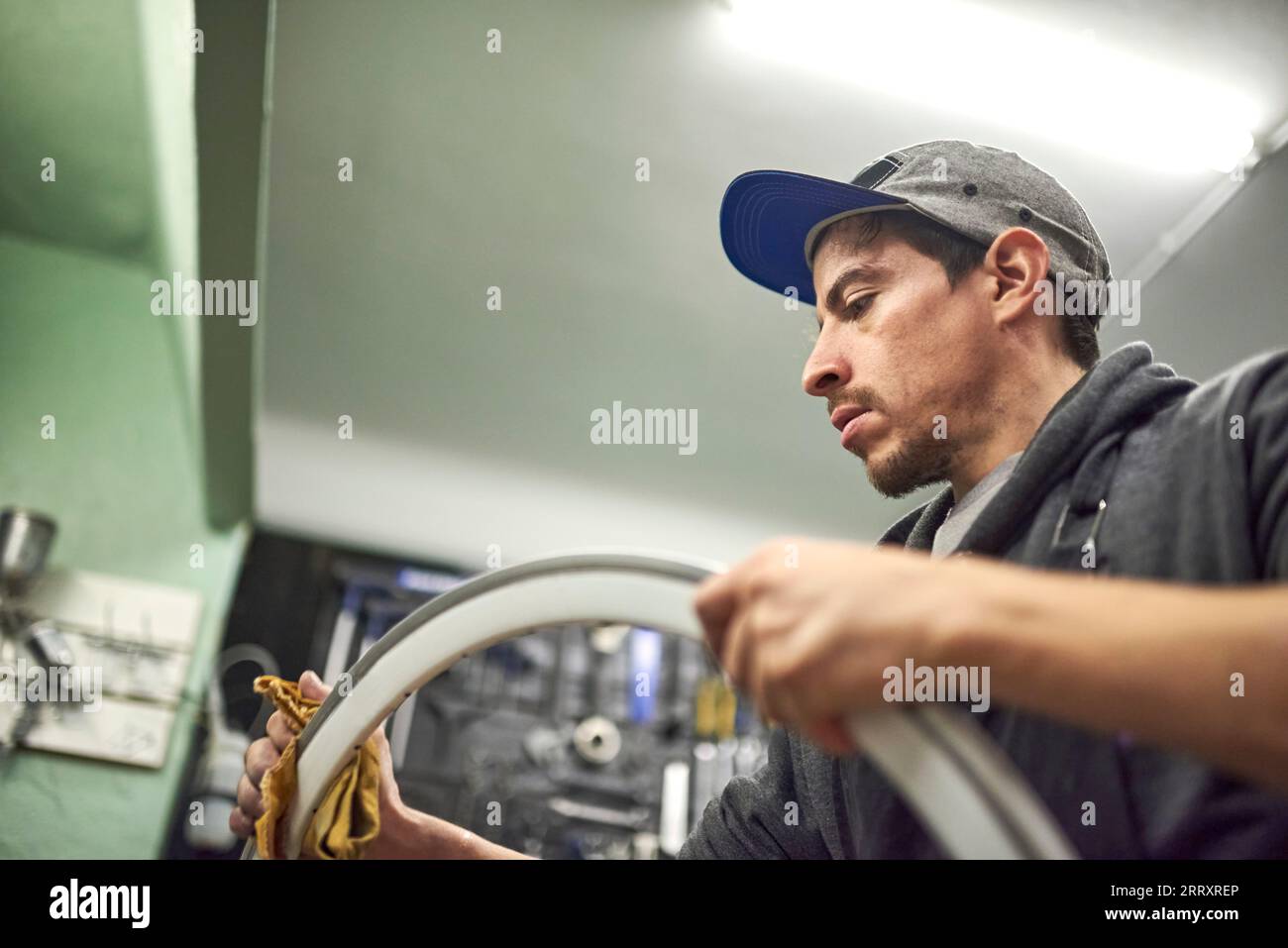 Uomo latino che prepara un cerchio di bicicletta da dipingere nella sua officina. Vista angolare bassa, composizione con spazio di copia. Foto Stock