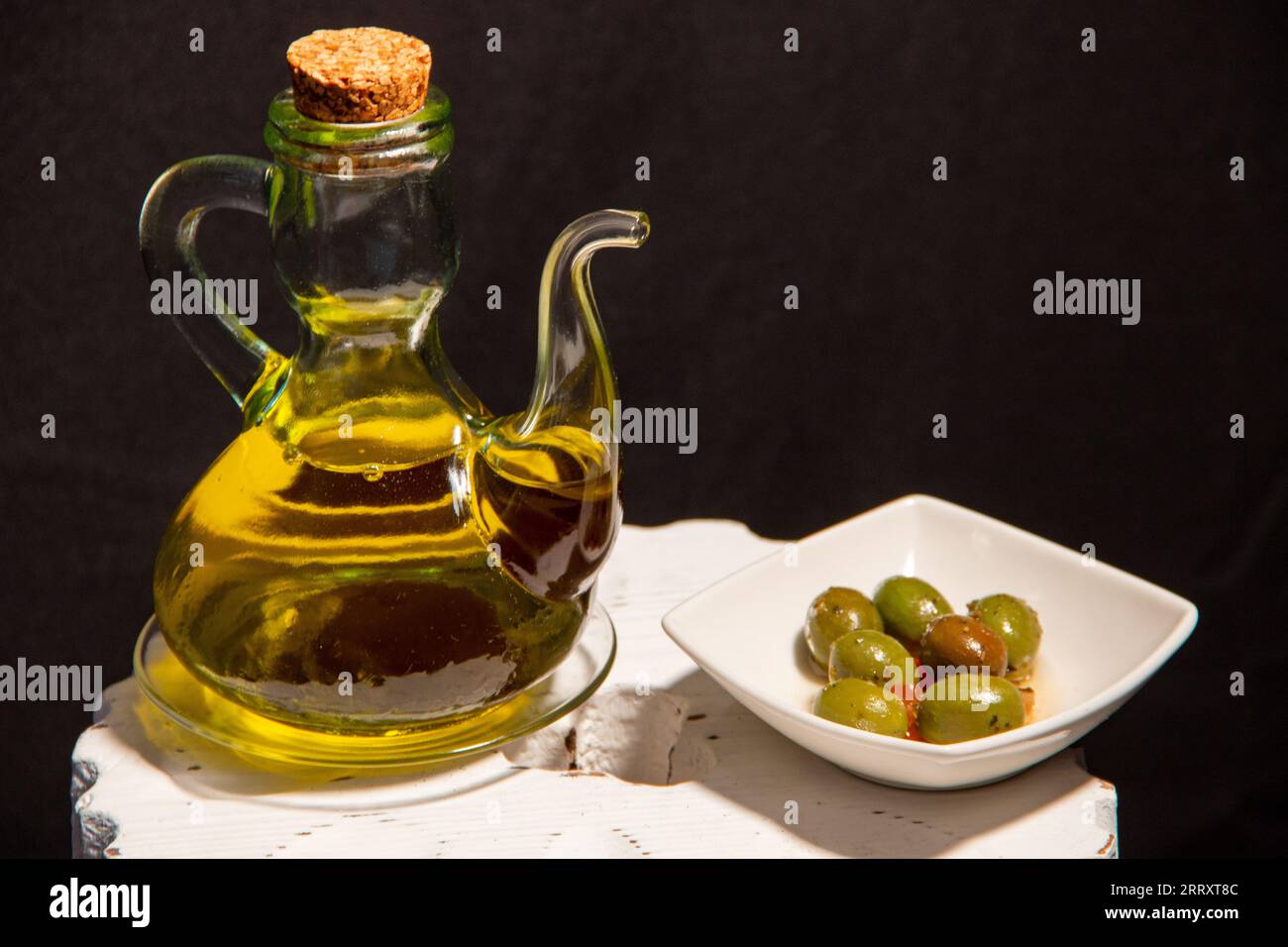 Spruzzo di olio extravergine d'oliva dalla Spagna, accanto a un piatto di olive verdi Foto Stock