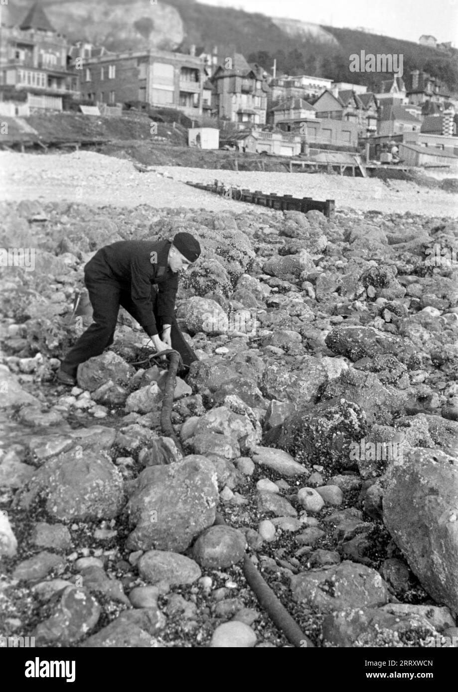 Ein jugendlicher Matrose der Kriegsmarine untersucht ein Stahlseil am Strand von le Havre, 1940. Un marinaio adolescente della Kriegsmarine esamina un cavo d'acciaio sulla spiaggia di le Havre, 1940. Foto Stock