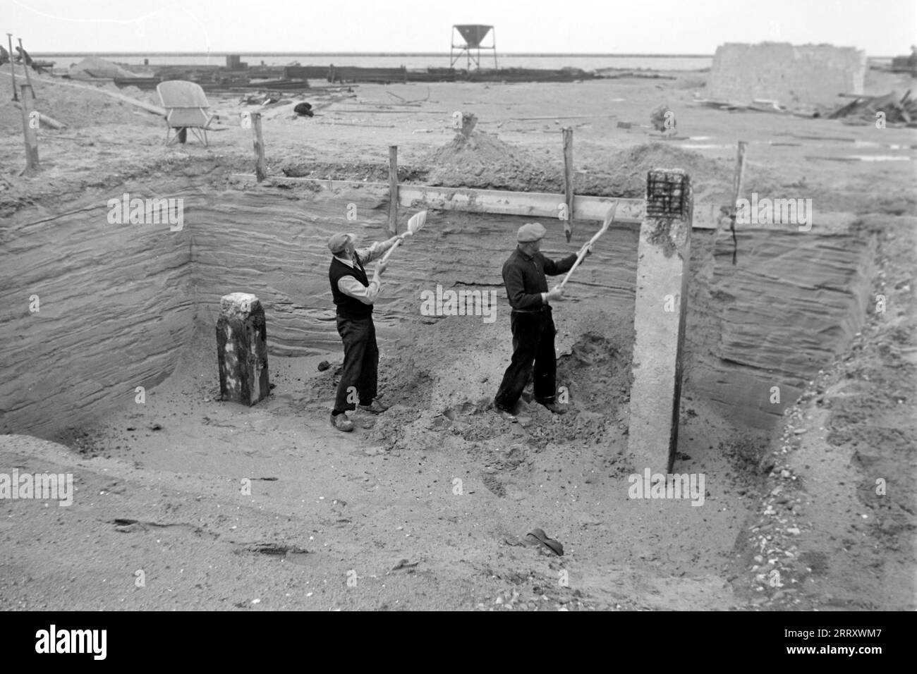Zwei Baurbeiter schaufeln Sand aus einer Grube auf der Baustelle von Lelystadhaven, 1955. Due operai edili lanciano la sabbia da una fossa nel cantiere di Lelystadhaven, 1955. Foto Stock