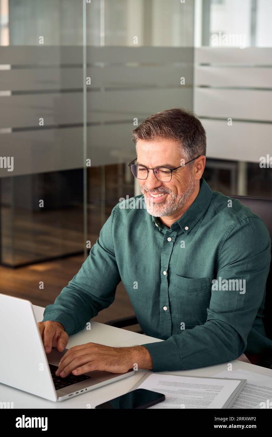 Uomo d'affari professionale maturo e sorridente che lavora su un notebook in ufficio. Foto Stock
