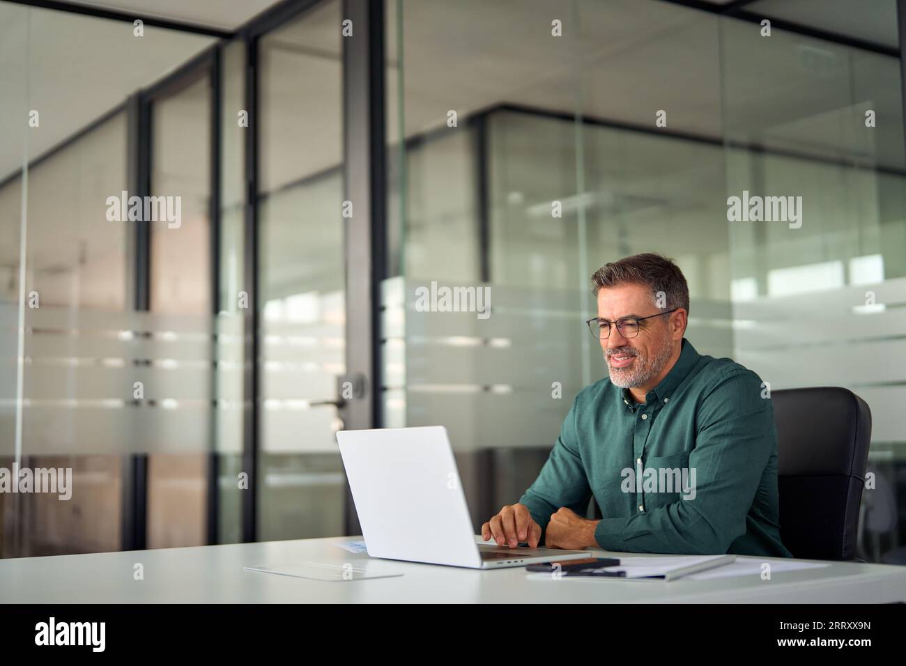 Un uomo d'affari anziano e sorridente che lavora su un computer portatile seduto alla scrivania. Foto Stock