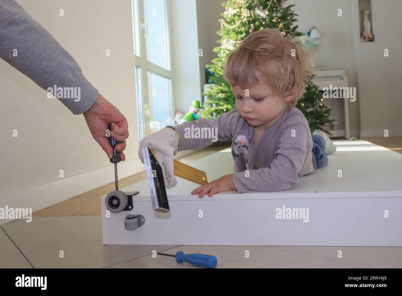 Papà e figlio stanno ristrutturando un letto a casa sullo sfondo di un albero di Natale. Foto Stock