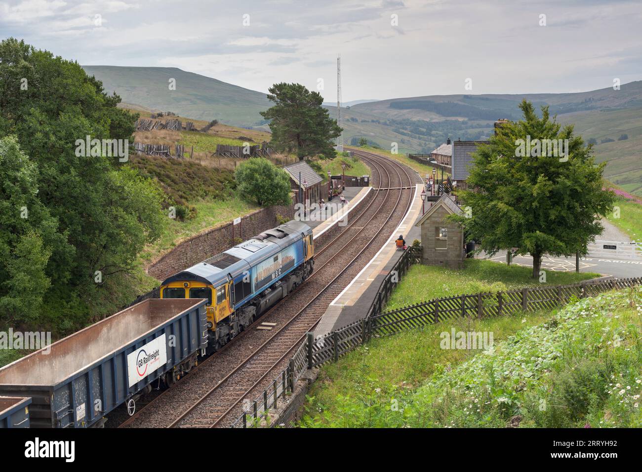 GB Railfreight classe 66 locomotiva diesel che trasporta un treno merci attraverso la stazione ferroviaria di Dent, Cumbria, Regno Unito sulla linea ferroviaria Settle to Carlisle Foto Stock