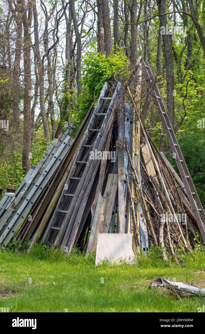 Un grande teepee è creato con legno di scarto e una varietà di scale, in questo cortile di campagna Foto Stock