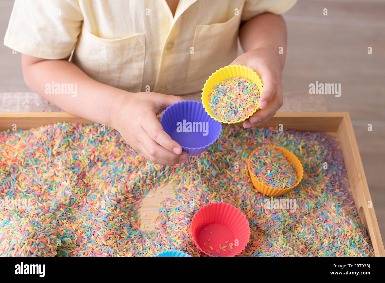 Bambini che giocano a mano con cestino sensoriale e tazze Foto Stock