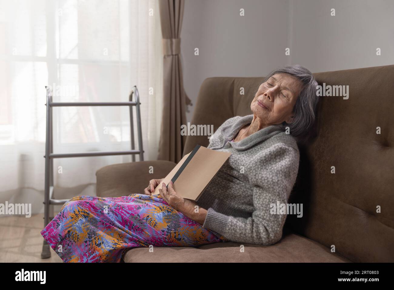 Anziana donna asiatica snooze mentre legge un libro su un divano. Foto Stock