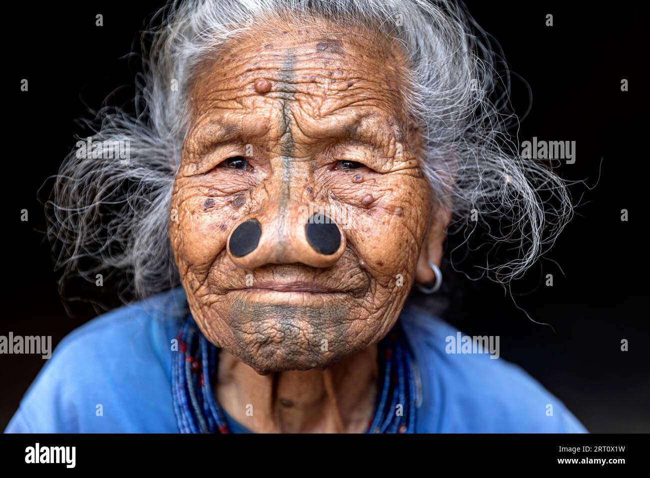 Donna della tribù degli apatani in una casa di un piccolo villaggio vicino a Ziro, con tradizionali tatuaggi facciali e tappi per naso tradizionali, Ziro, India Foto Stock