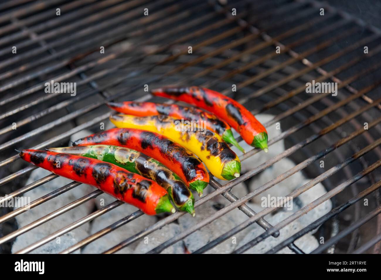 Primo piano di peperoni caldi multicolori adagiati sulla griglia di cottura del barbecue al carbone Foto Stock