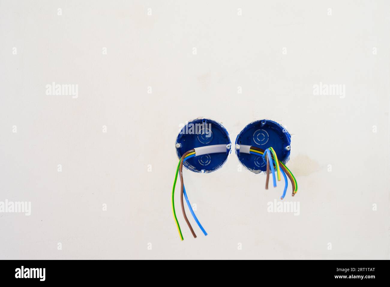 Preparazione all'installazione della presa a muro. I fili elettrici fuoriescono dal foro della presa elettrica su una parete grigia in cemento. Foto Stock