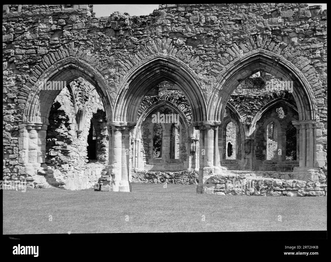 Fountains Abbey, Harrogate, North Yorkshire, 1940-1949. Una vista delle rovine dell'Abbazia di Fountains vista attraverso un trittico di archi in primo piano. Gli archi sono disposti in pietra affrescata che è danneggiata in cima e rivelano bassi muri di pietra direttamente dietro di loro. Più avanti sullo sfondo ci sono più file di archi sia paralleli che perpendicolari alla parte anteriore. L'abbazia fu fondata nel 1132 dai monaci cistercensi ed è una delle più belle abbazie conservate. L'edificio principale ebbe luogo tra il 1170-1247 e la fine del XV secolo e l'inizio del XVI secolo. L'abbazia aveva molti proprietari dopo lo scioglimento ed è attualmente di proprietà Foto Stock