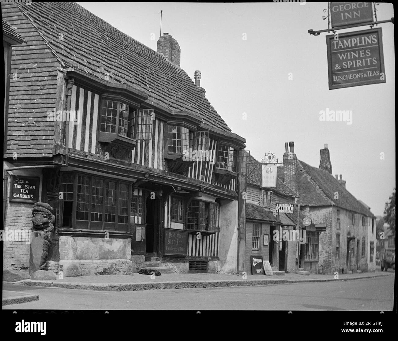 The Star Inn, High Street, Alfriston, Wealden, East Sussex, 1940-1949. Una vista sulla strada di High Street ad Alfriston con un focus sullo Star Inn, sul lato sinistro dell'immagine. L'inn è un edificio del XV secolo con struttura in legno con intonaco e un piano superiore con gesso con tre finestre. All'estrema sinistra c'è un palo con un animale intagliato. A destra della locanda ci sono altri due edifici elencati: Il primo è la Saddler's House e la Ye Olde Tea House, che ha cartelli appoggiati contro l'edificio e un cartello appeso sulla porta; e il secondo, più avanti sullo sfondo, è Patricia Okel Foto Stock