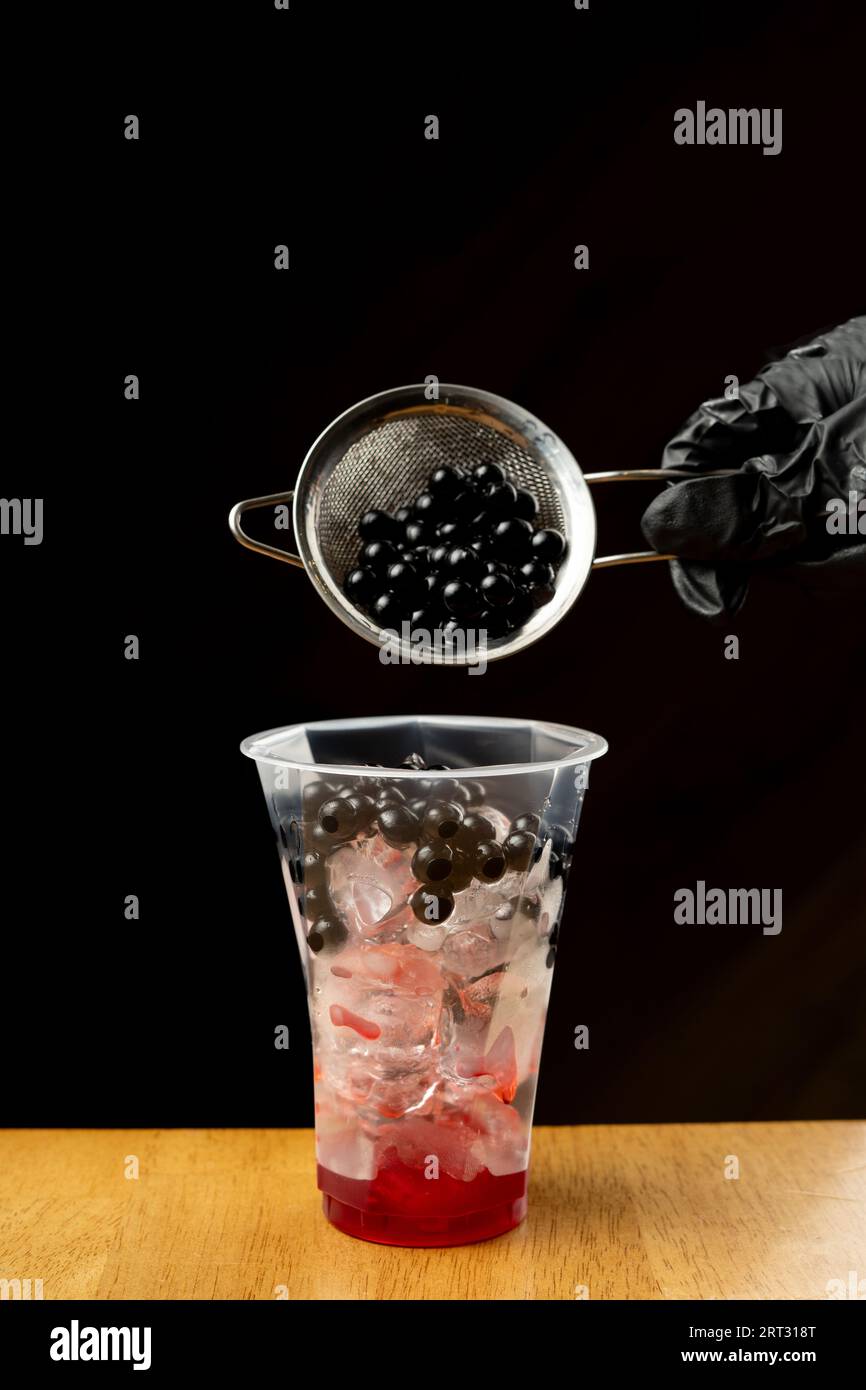 Versare mini perle di boba marrone in un bicchiere di plastica di tè al latte freddo Foto Stock