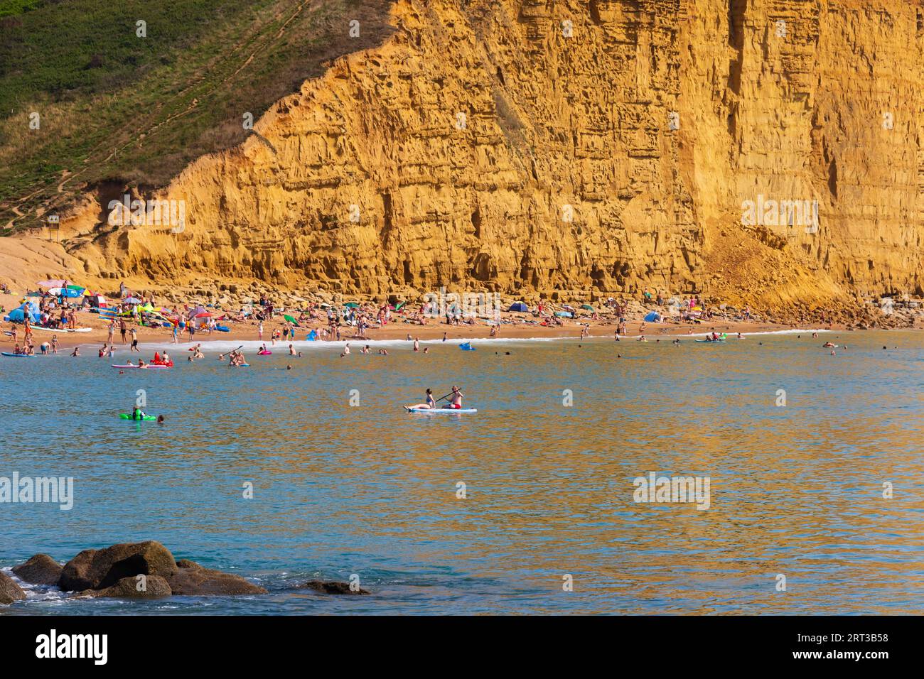 Le scogliere dorate di West Bay con bagnanti e nuotatori dopo la recente caduta di rocce rupestri. Bridport, Dorset. Il giorno più caldo dell'anno. Foto Stock