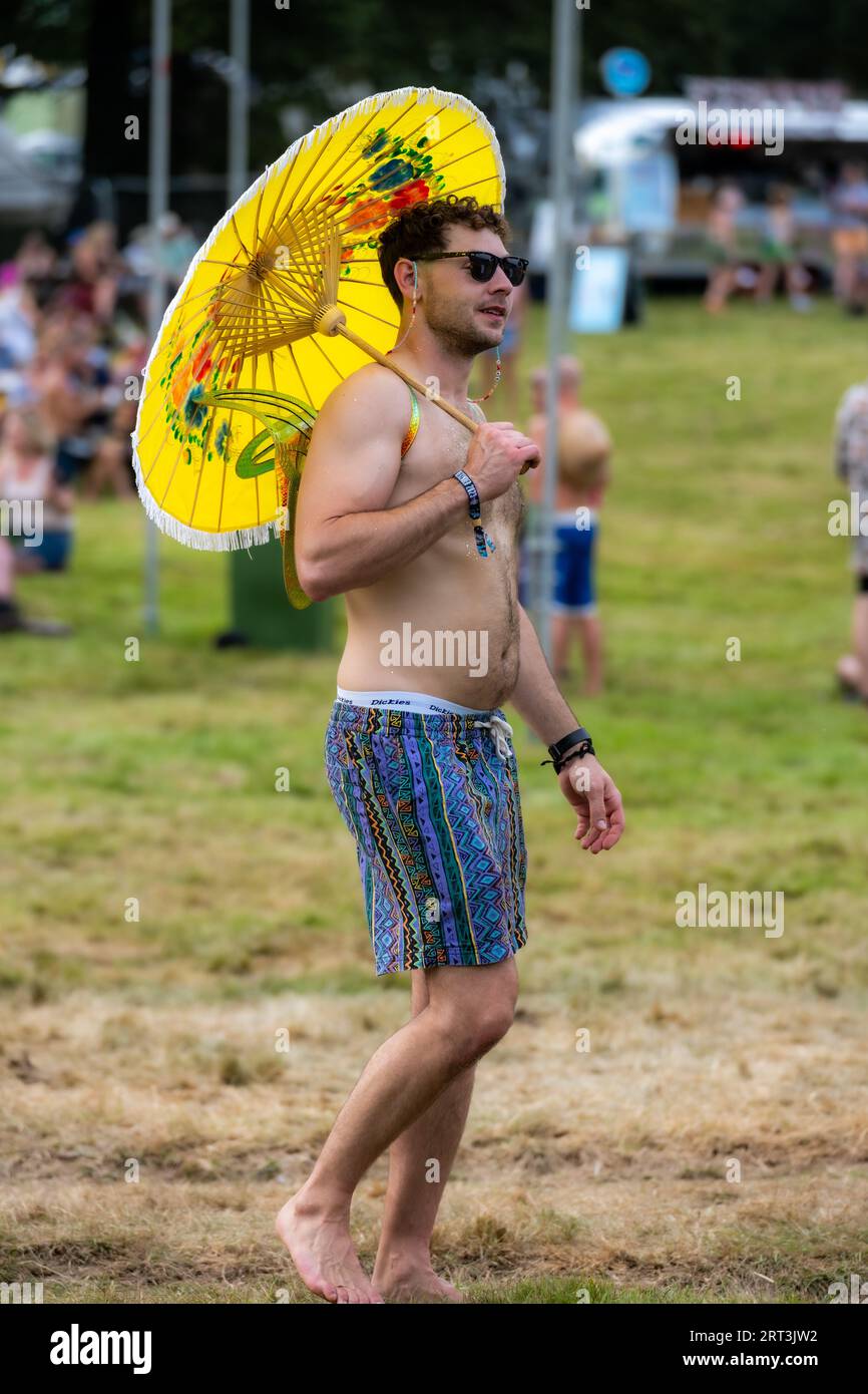 Mantenersi fresco con un ombrello giallo come ombrellone. Mucky Weekender Festival, Vicarage Farm, Woodmancott, vicino a Winchester, Hampshire, REGNO UNITO Foto Stock