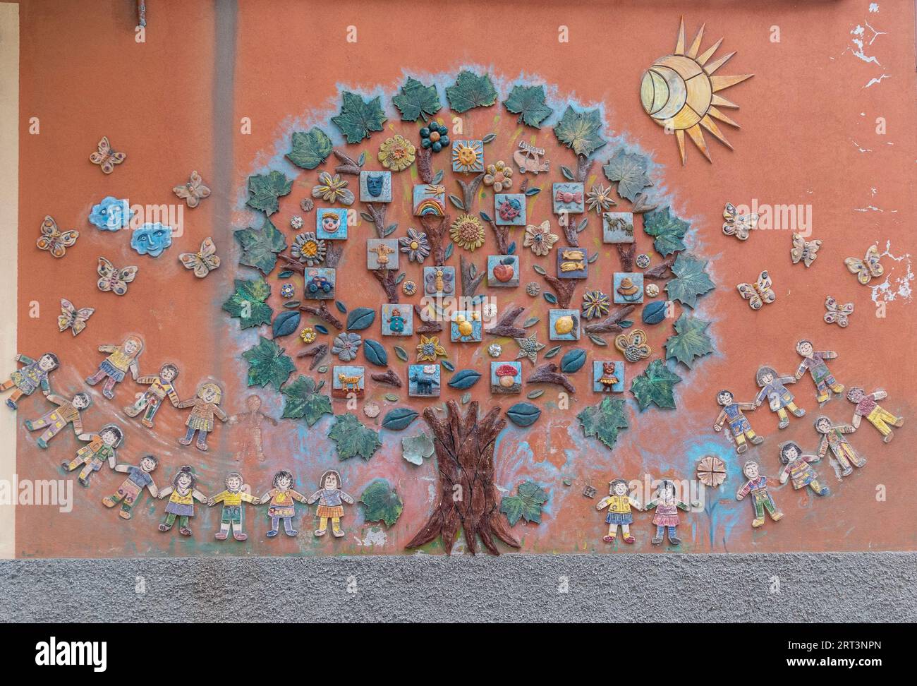 Dettaglio di una decorazione murale in ceramica sulla facciata di un asilo che raffigura un grande albero circondato da bambini, Savona, Liguria, Italia Foto Stock