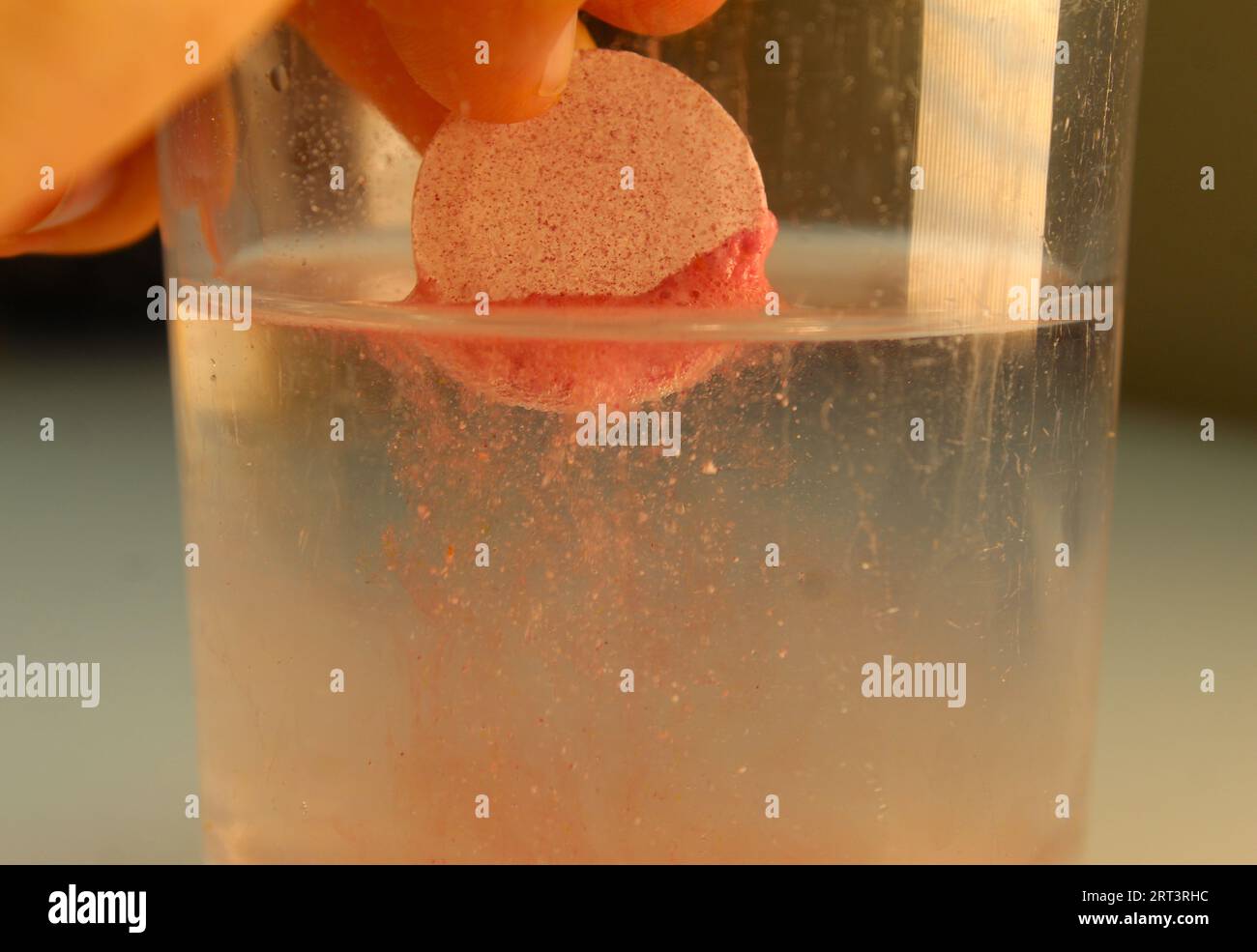 Una foto di una compressa di elettrolito rosa che si dissolve in un bicchiere d'acqua. Foto Stock